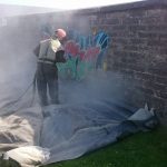 man sandblasting graffitied wall